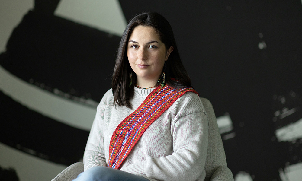 Hanna Paul against a black and white background wearing an Indigenous multi-coloured sash